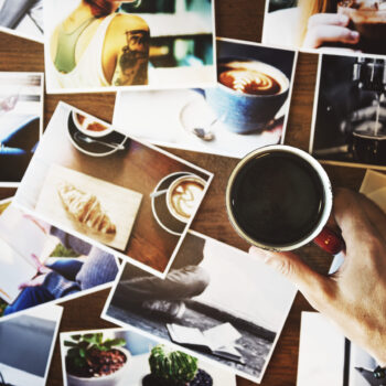 Hand holding coffee cup with may photograph on the table